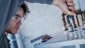 Person wearing safety equipment tightens a screw on a metal panel.