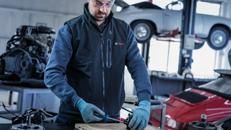 Person wearing safety equipment uses a power tool on a table in an auto repair shop.