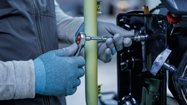 Person wearing safety equipment tightens a bolt on metal machinery with a ratchet.