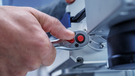 Person adjusts a metallic tool using a ratchet with red buttons.