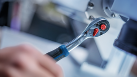 Person using a ratchet wrench to fasten a bolt on industrial machinery.