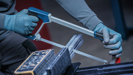 Person wearing safety equipment cuts metal with a hacksaw in a vise.