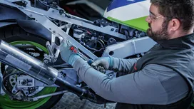 Person wearing safety equipment fastens a bolt on a motorcycle frame.