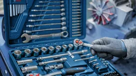Person wearing safety equipment holds a ratchet above a socket wrench tool set.