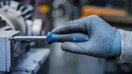 Person wearing safety equipment tightens a machine part with a screwdriver.