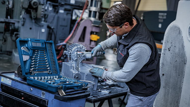 Person wearing safety equipment tightens a bolt on machinery with a ratchet tool.