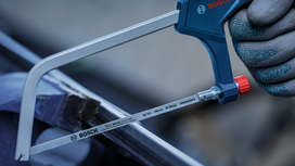 Person wearing safety equipment uses a handheld saw to cut a metal bar.