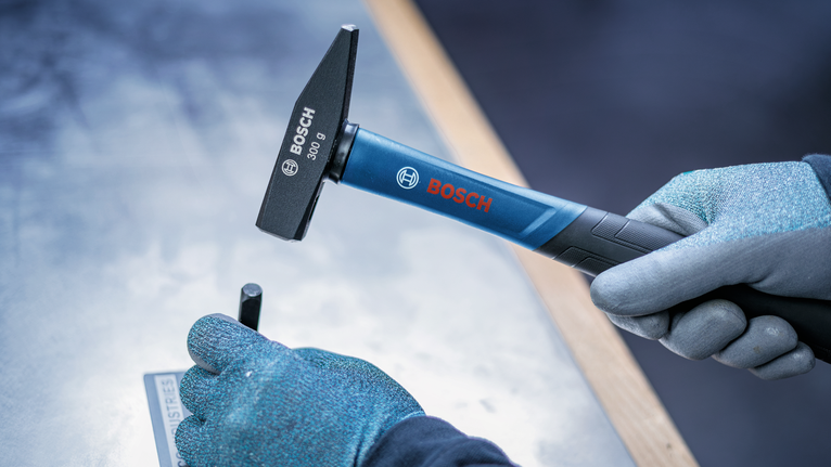 Person wearing safety equipment uses a hammer and punch to mark metal.