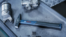 Hammer with a blue handle rests on a metal workbench beside automotive components.