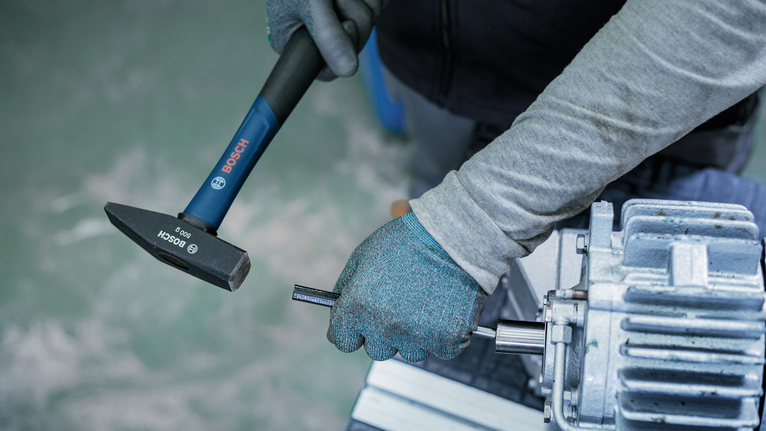Person wearing safety equipment uses a hammer to adjust a metal component.