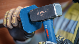 Person wearing safety equipment strikes a metal chisel with a heavy hammer.