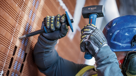 Person wearing safety equipment chisels a brick wall with a hammer and chisel.
