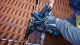 Person wearing safety equipment uses a hammer and chisel to shape a brick wall.