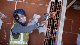 A person wearing safety equipment breaks a wall brick with a hammer.