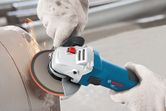 A person wearing safety equipment operates an angle grinder to cut metal, producing sparks.