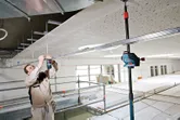 A person wearing safety equipment aligns ceiling framework using a laser leveling tool.