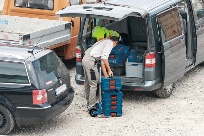 Aluminium Caddy A person loading stacked toolboxes onto a collapsible hand truck beside a van.