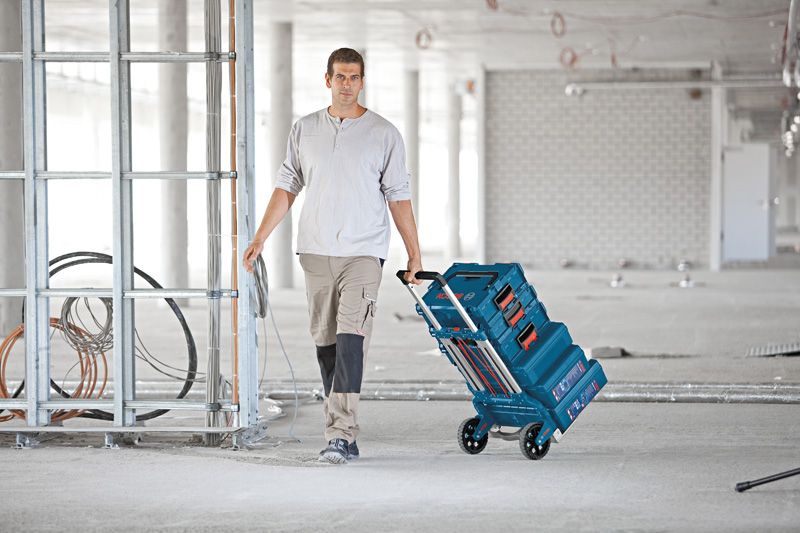 Aluminium Caddy A person pulls a collapsible hand truck with stacked toolboxes in a construction area.