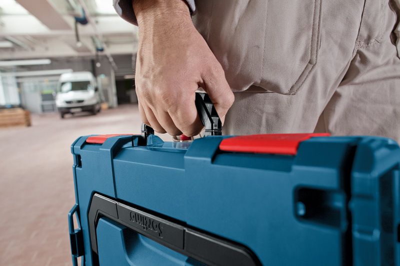 Person carrying a blue tool case in a workshop area.