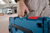 Person carrying a blue tool case in a workshop area.