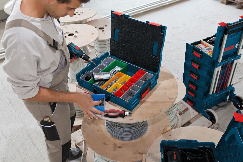 A person organizes fasteners in a toolbox on a cable spool in a workshop.