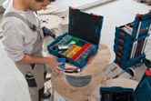 A person organizes fasteners in a toolbox on a cable spool in a workshop.