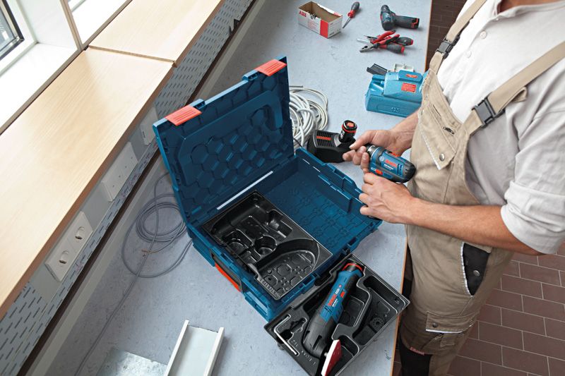 A person wearing safety equipment prepares a cordless drill at a workstation.