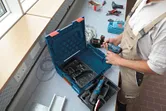 A person wearing safety equipment prepares a cordless drill at a workstation.