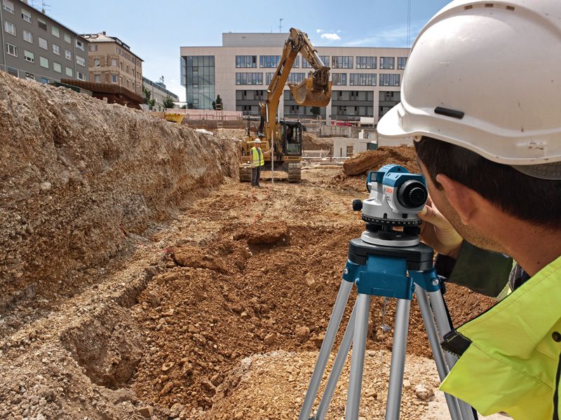 GOL 32 D Person wearing safety equipment uses a surveyor level at a construction excavation site.