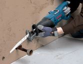 A person wearing safety equipment uses a reciprocating saw to cut a metal pipe.