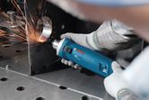 A person wearing safety equipment grinds a metal edge with an electric tool, creating sparks.