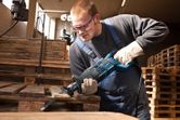 A person wearing safety equipment uses a reciprocating saw to cut a wooden pallet.