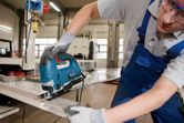 A person wearing safety equipment guides a jigsaw to cut a sheet of metal.