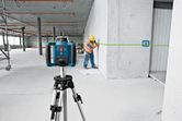 A person wearing safety equipment marks a wall using a green laser leveling tool.