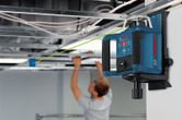 Laser leveling tool projecting a green line as a person installs a suspended ceiling.