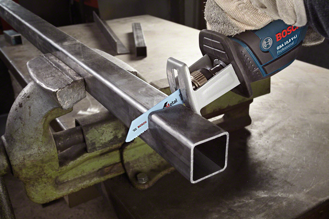 Person wearing safety equipment cuts a metal pipe clamped in a vise with a reciprocating saw.