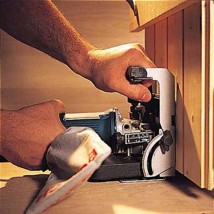 Person wearing safety equipment operates a jointer on a wood surface near a wall.