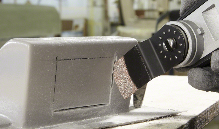 Oscillating tool cuts a precise rectangle in a metal box, worker wearing safety equipment.