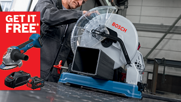 A Bosch Professional compound miter saw is on a workbench, with a man in a black jacket operating it. A promotional banner in red and white says 'GET IT FREE' with images of a blue angle grinder and battery. The setting is industrial, with metal surfaces and tools nearby.