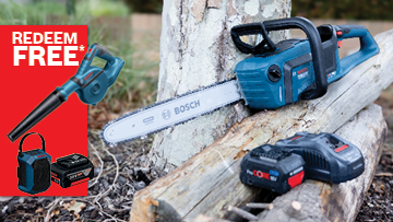 A blue Bosch Professional chainsaw rests on a log, with a battery pack and promotional items nearby.