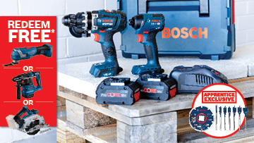 A set of Bosch Professional power tools, including a drill and an impact driver, displayed on wooden pallets with batteries and a toolbox in the background.