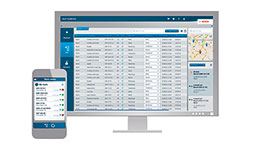 A computer monitor displays a software interface with data tables and a mobile phone beside it.